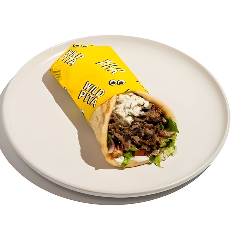 Wild Pita gyro with meat, lettuce, and sauce, partially wrapped in yellow paper, on a white plate.