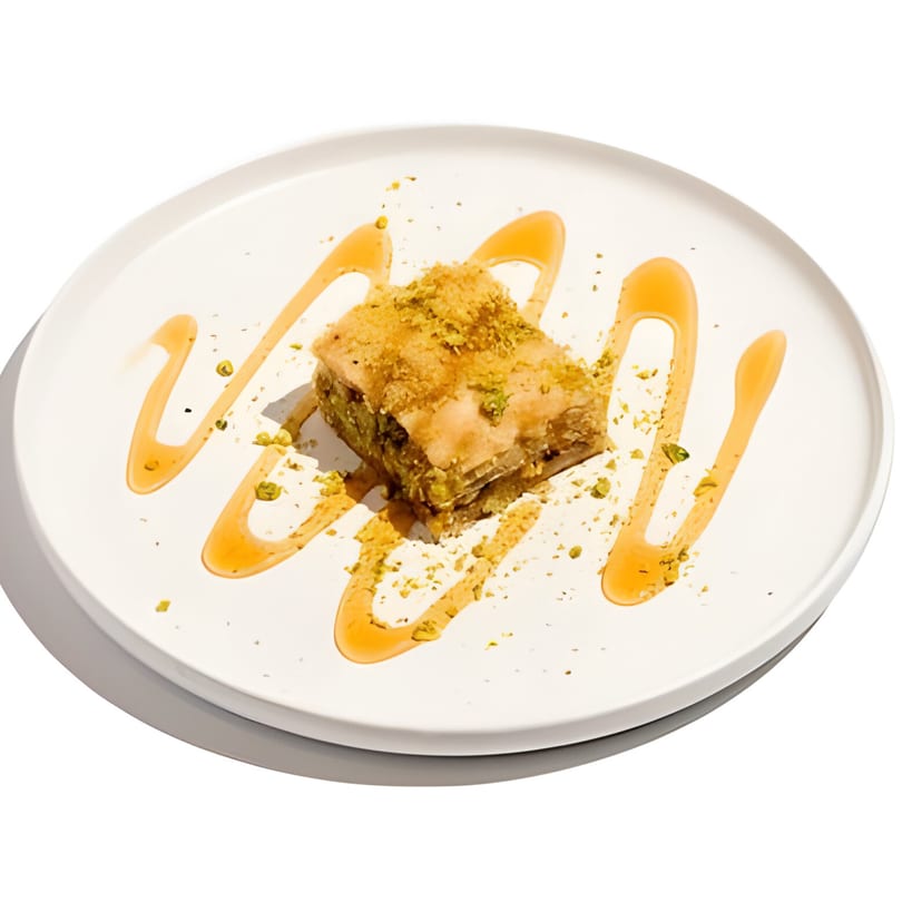 Wild Pita's baklava, a golden pastry square drizzled with honey and sprinkled with pistachios on a white plate.