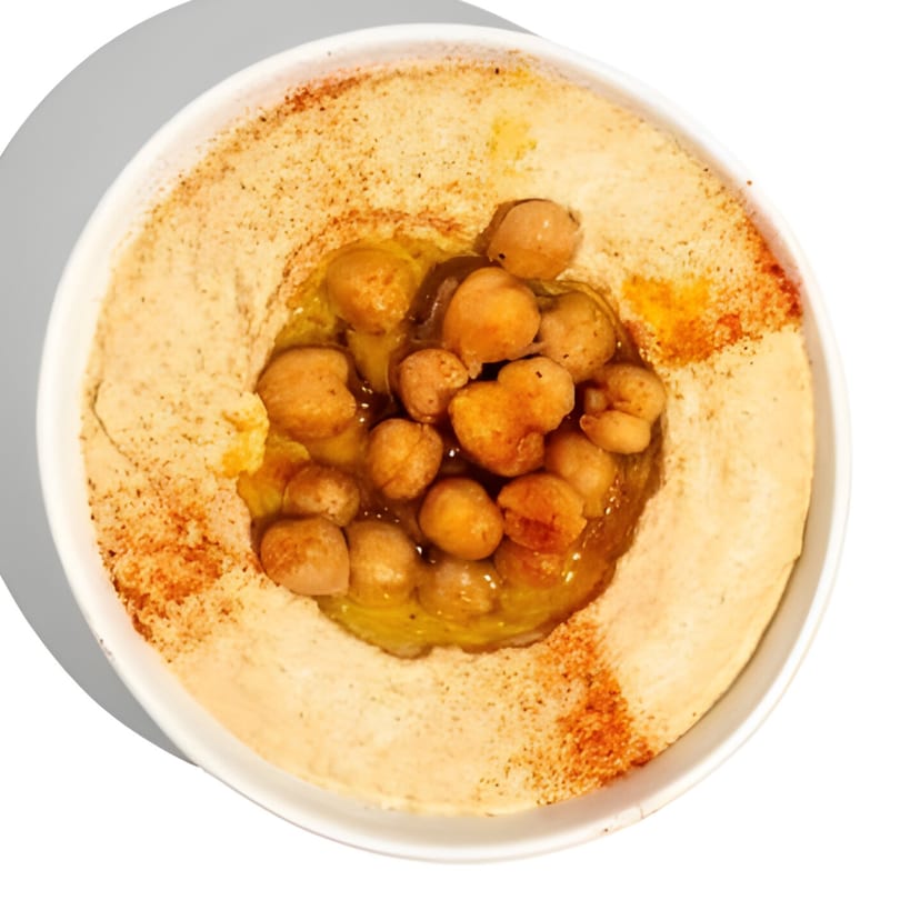 Creamy hummus topped with whole chickpeas, olive oil, and a sprinkle of paprika in a white bowl.
